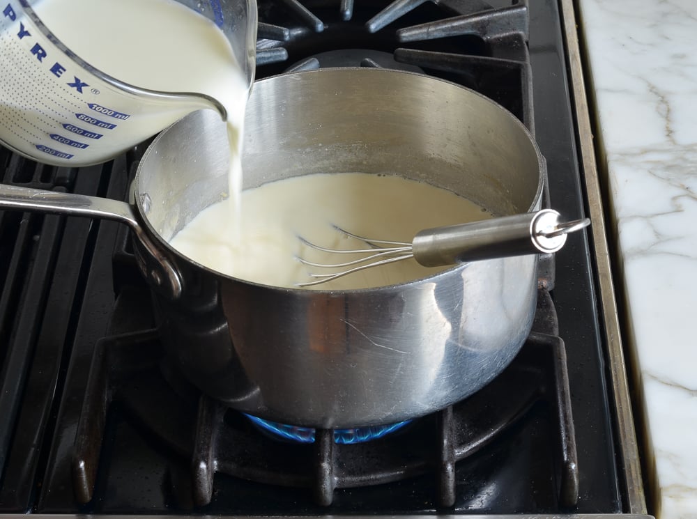 Half and half pouring into a pot on a stovetop.