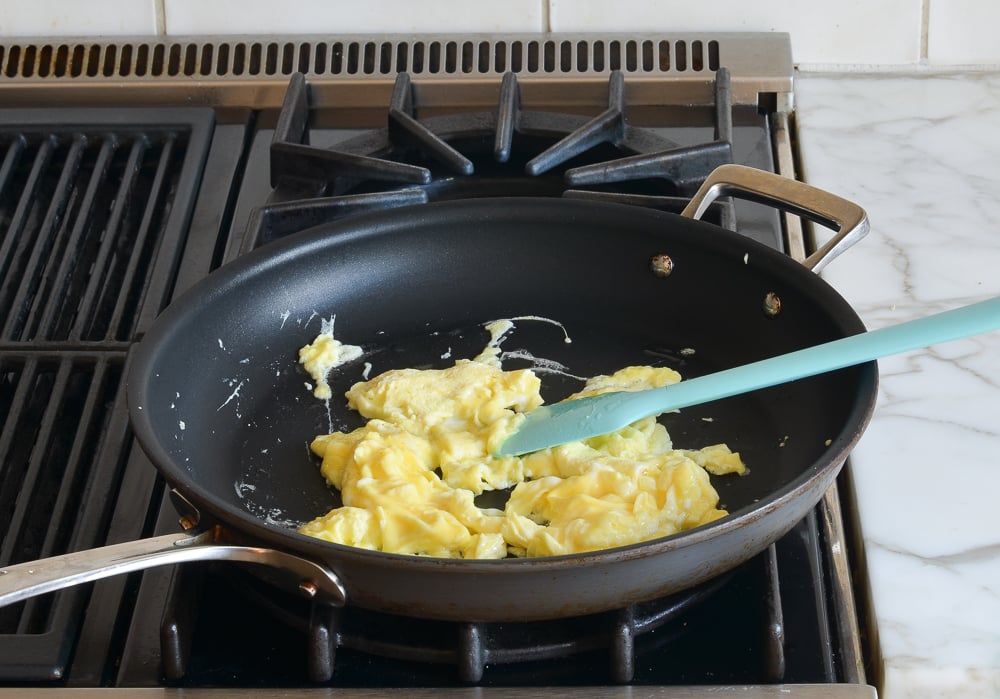 Spatula scrambling egg in a skillet.