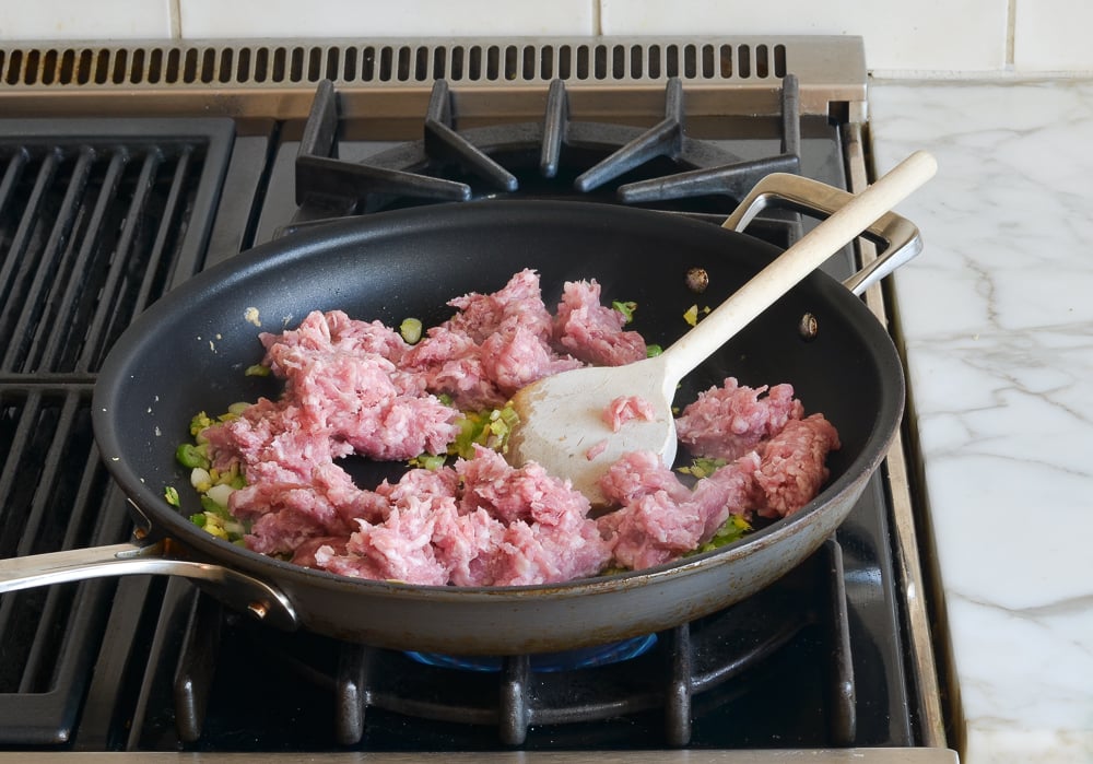 Ground pork in a skillet with vegetables.