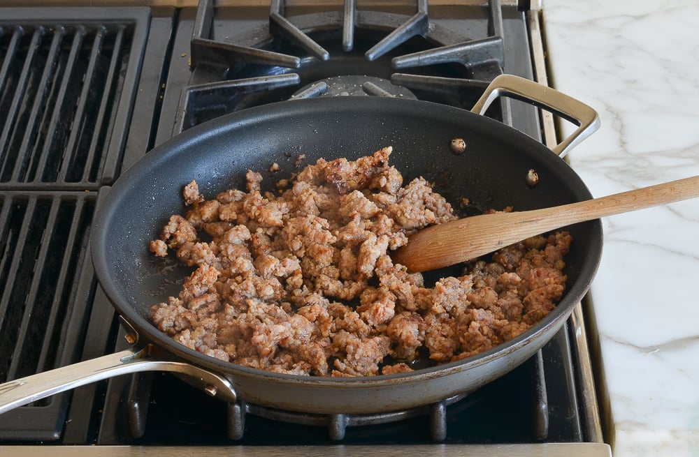 breaking apart the sausage with a spoon