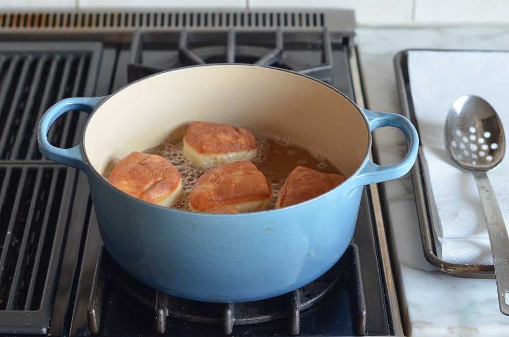 Pieces of dough frying in oil in a Dutch oven.
