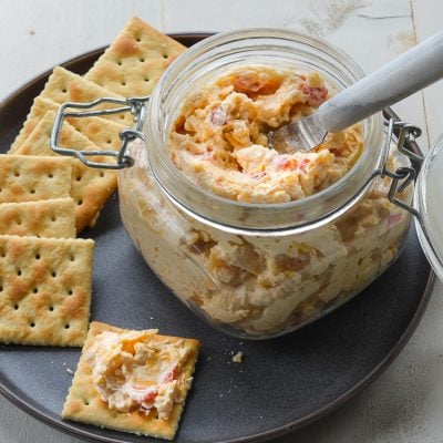 Jar of pimento cheese on a plate with crackers.