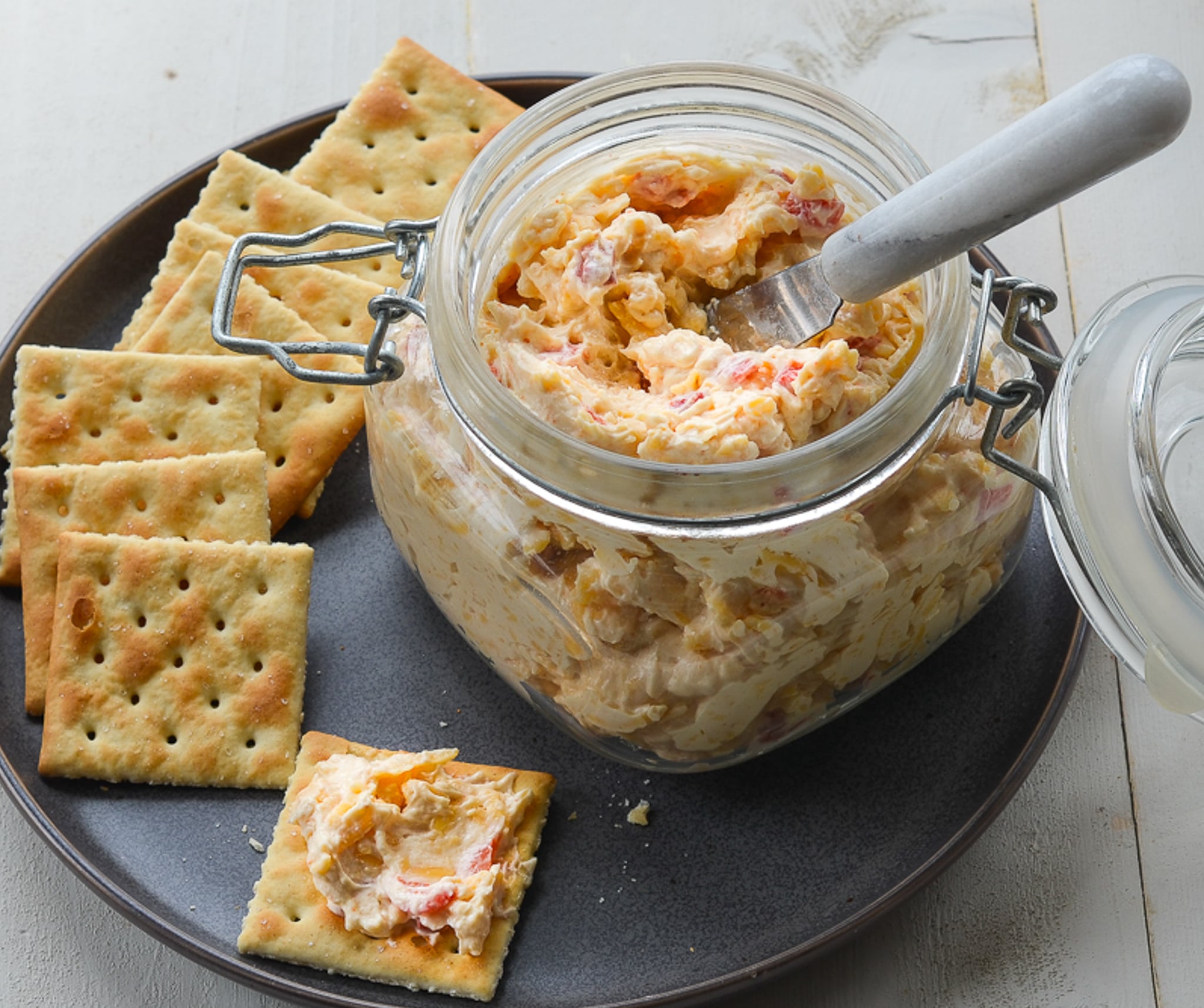 Jar of pimento cheese on a plate with crackers.