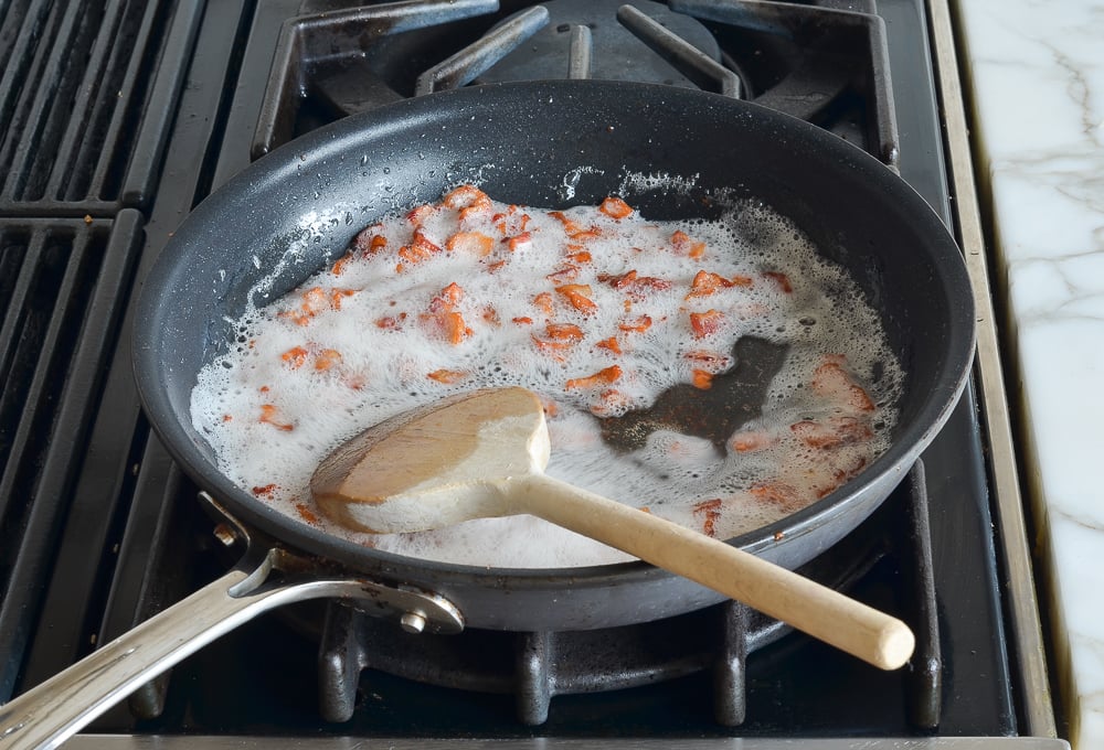 Diced bacon cooking in a skillet.