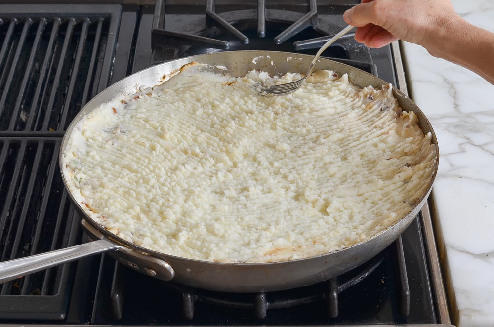 using a fork to make ridges on the mashed potatoes
