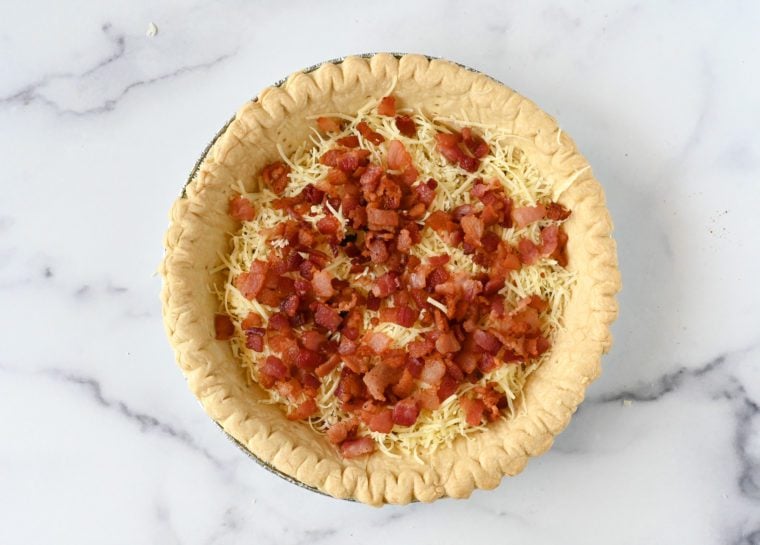 Diced bacon on shredded gruyere in a pie crust.