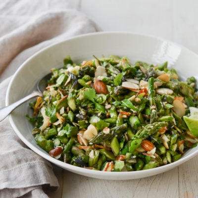 Spoon in a bowl of raw asparagus salad with almonds and ginger-sesame vinaigrette.