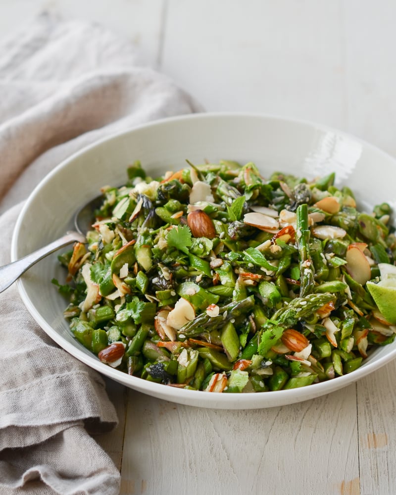 Spoon in a bowl of raw asparagus salad with almonds and ginger-sesame vinaigrette.