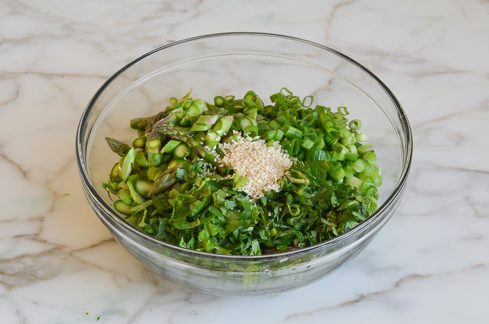 asparagus, scallions, herbs, and sesame seeds in mixing bowl