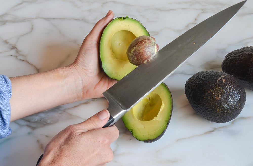 A woman's hands demonstrating how to pit an avocado.