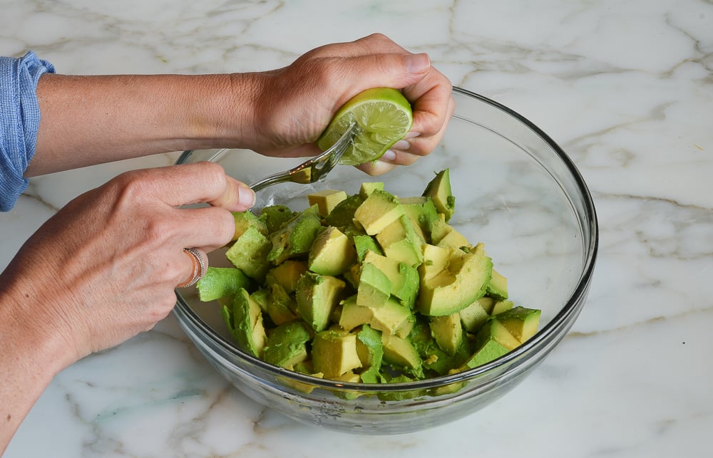 Squeezing lime over avocado in a bowl.