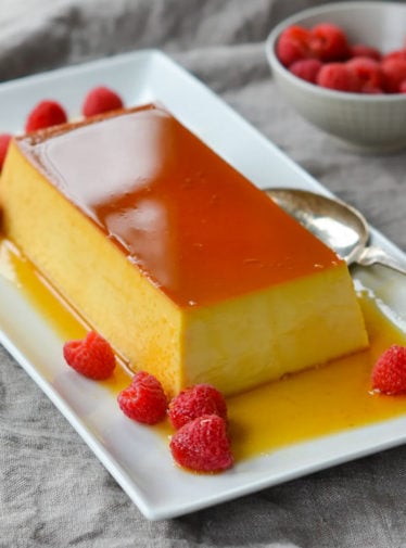 Best flan recipe served on a rectangle platter with raspberries.