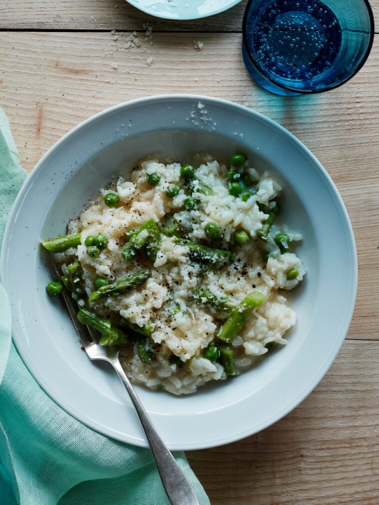 Risotto recipe in bowl with Parmesan cheese and glass of sparkling water.