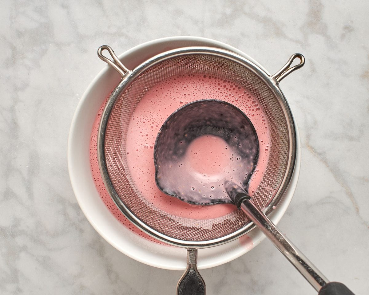 straining the seeds from the strawberry frozen yogurt base