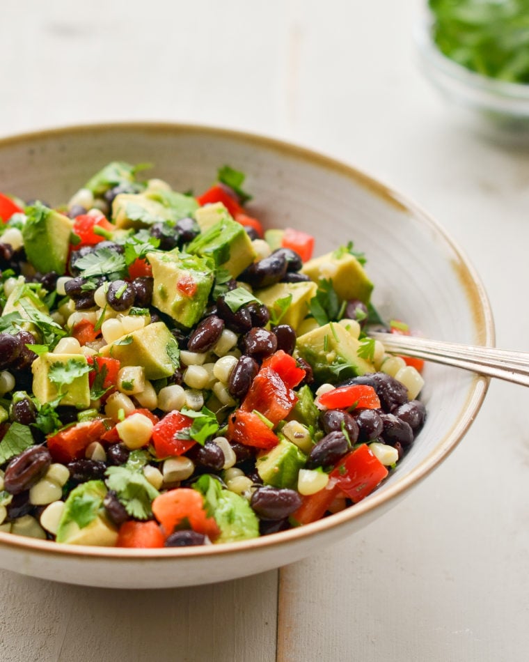 Spoon in a bowl of black bean salad with corn, avocado, and lime vinaigrette.
