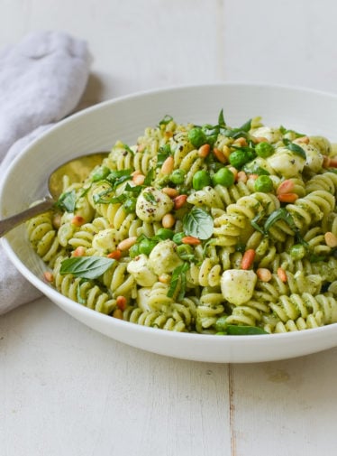Bowl of pesto pasta salad with pea, pine nuts, and mozzarella pearls.