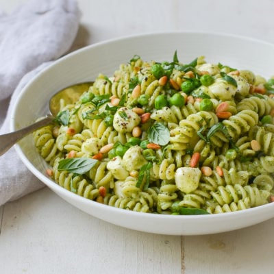 Bowl of pesto pasta salad with pea, pine nuts, and mozzarella pearls.
