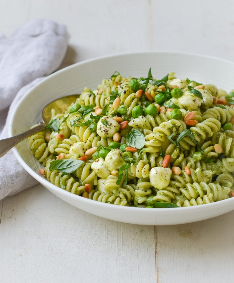 Bowl of pesto pasta salad with pea, pine nuts, and mozzarella pearls.