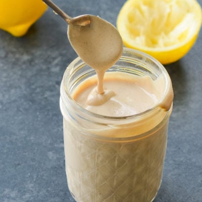 Spoon dripping tahini sauce into a glass jar.
