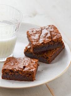Three brownies on a plate with a glass of milk.
