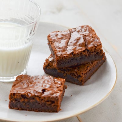 Three brownies on a plate with a glass of milk.