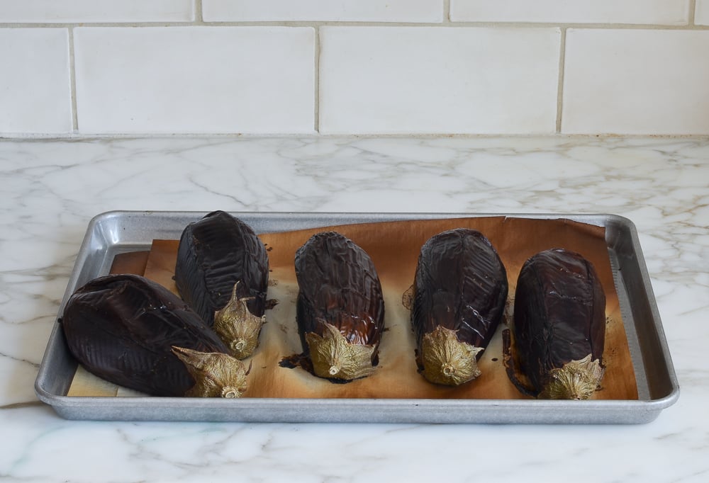 Roasted eggplants on a lined baking sheet.