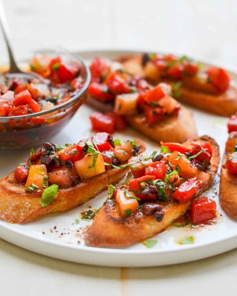 Plate of bruschetta with heirloom tomatoes, olives, and basil.