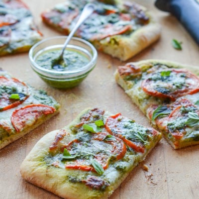 Slices of pesto pizza with fresh tomatoes and mozzarella on a wooden board.