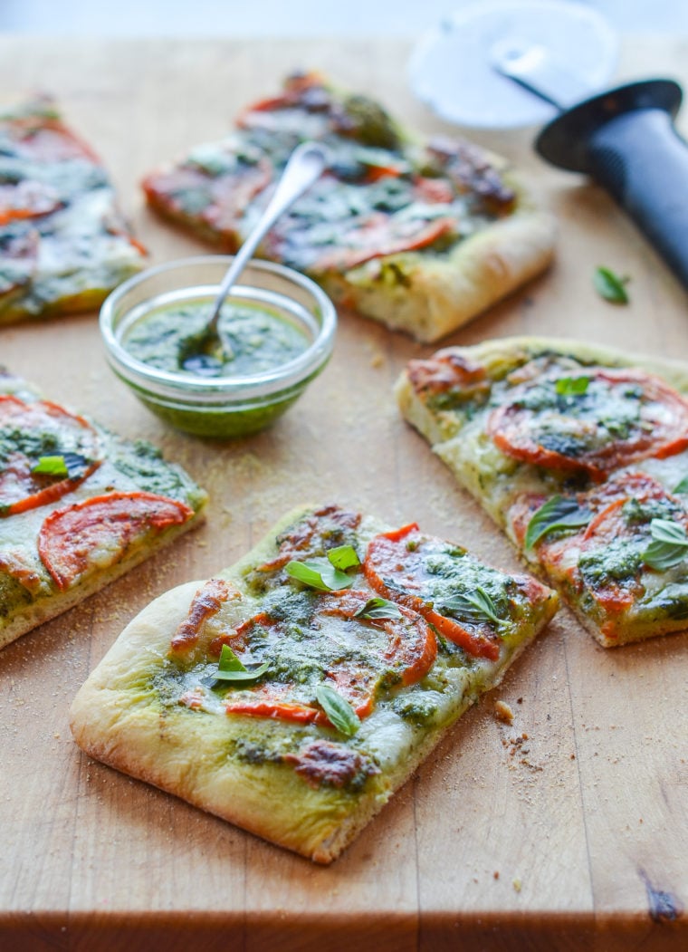 Slices of pesto pizza with fresh tomatoes and mozzarella on a wooden board.
