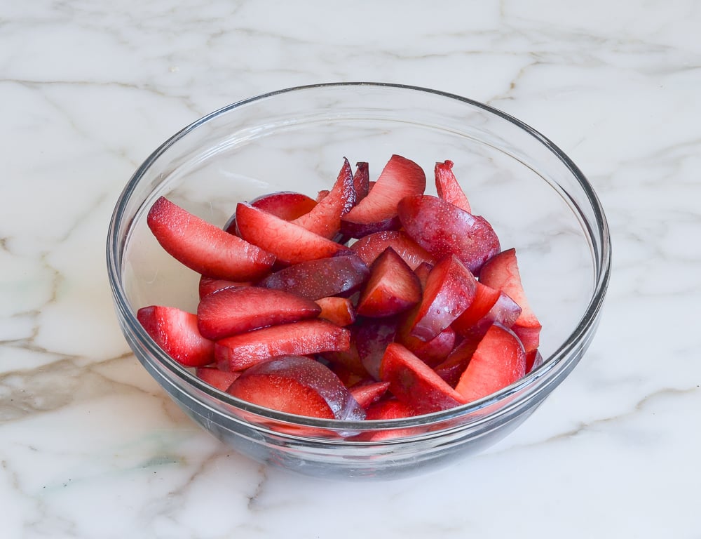 Glass bowl of sliced plums.