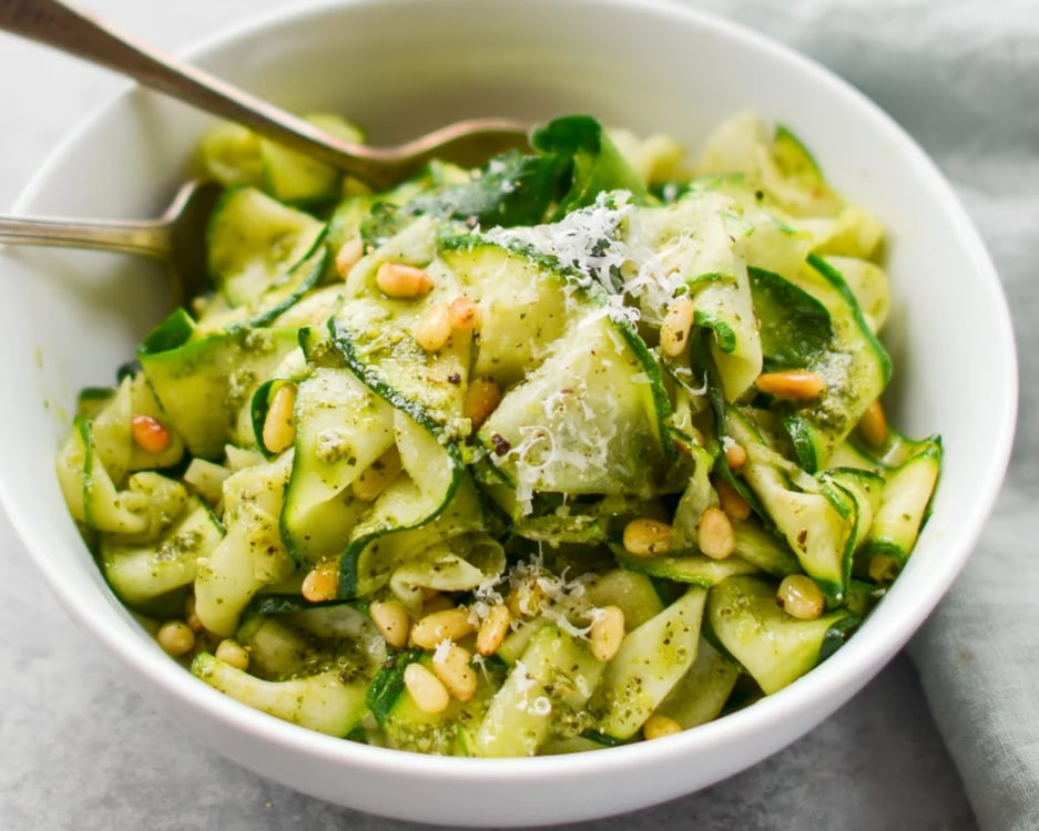 Zucchini noodles in white bowl with serving spoons.