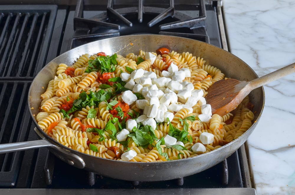 adding the cheese and basil to the pasta
