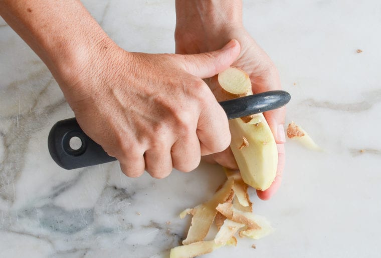 Person peeling ginger with a vegetable peeler.