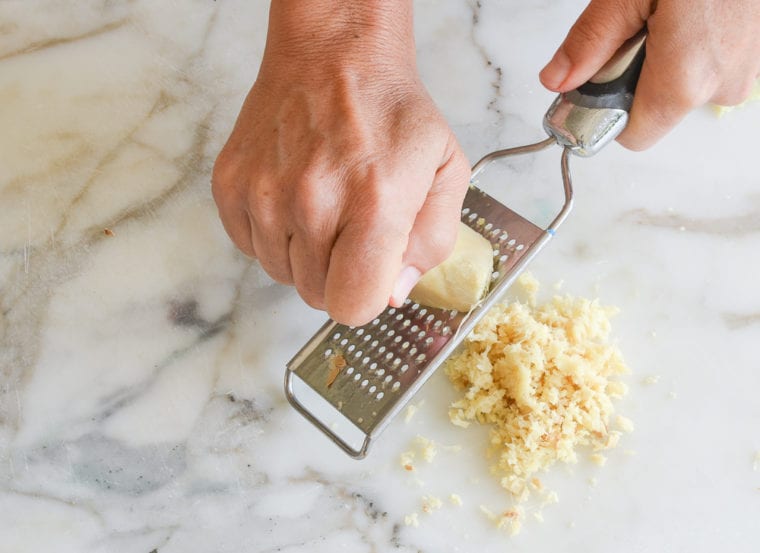 Person grating ginger onto a counter top.