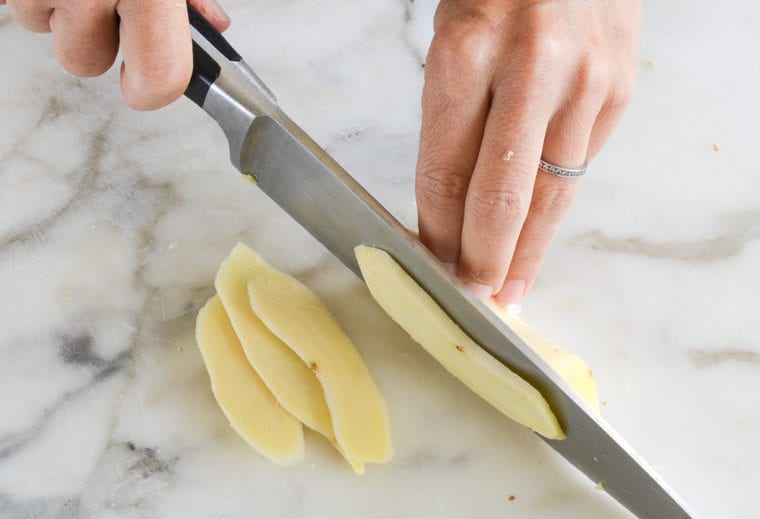 Person slicing ginger with a knife.