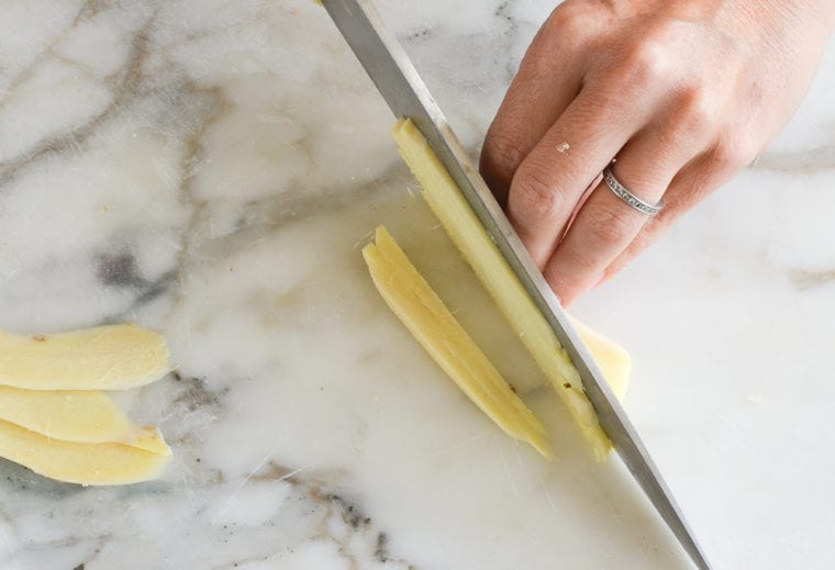 Person julienning ginger with a knife.