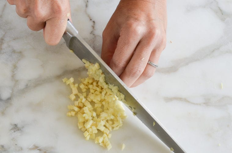 Person dicing ginger with a knife.