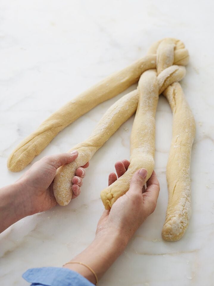 Person grabbing the two middle strands of challah dough out of four.