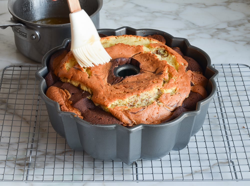 Brush putting glaze on a marble cake in a Bundt pan.