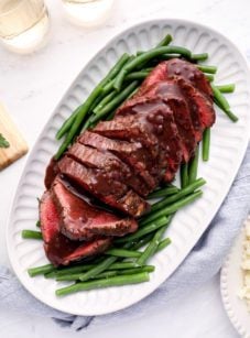 Roast beef tenderloin on a platter with green beans.