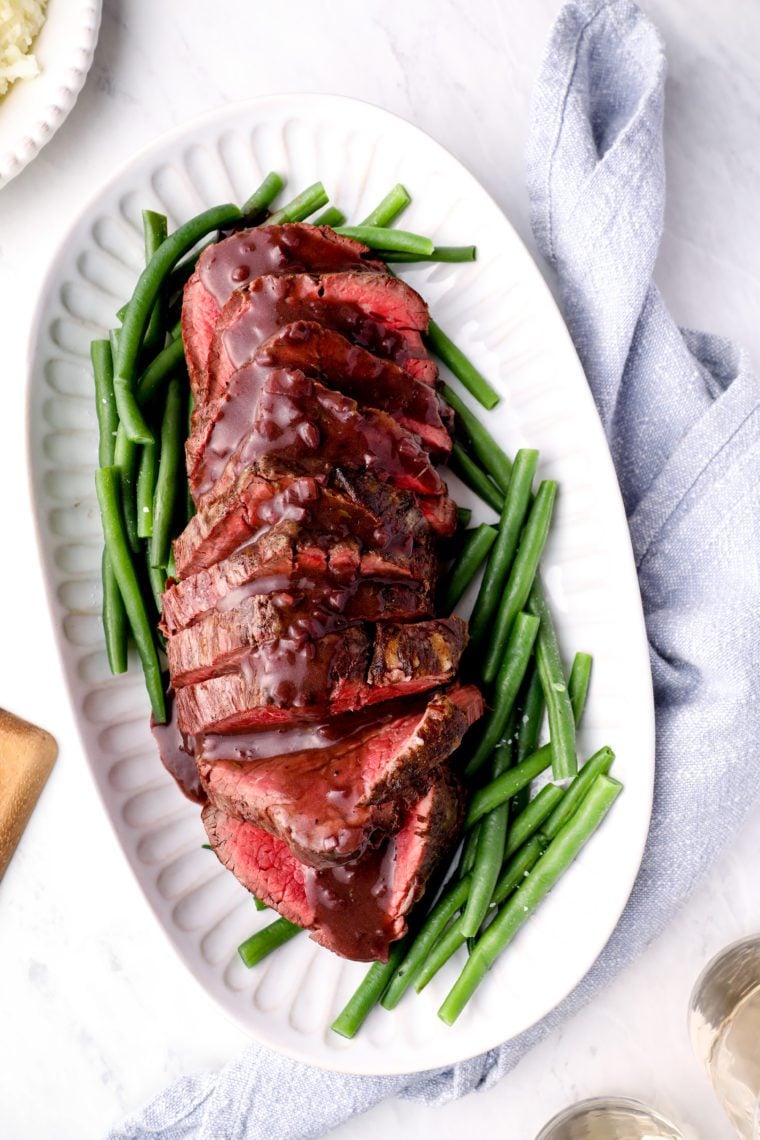 Platter of roast beef tenderloin with red wine sauce over green beans.