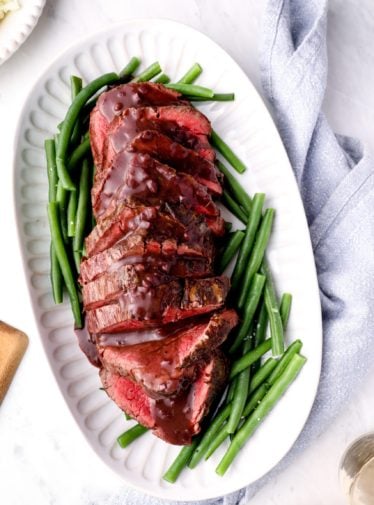 Platter of roast beef tenderloin with red wine sauce over green beans.