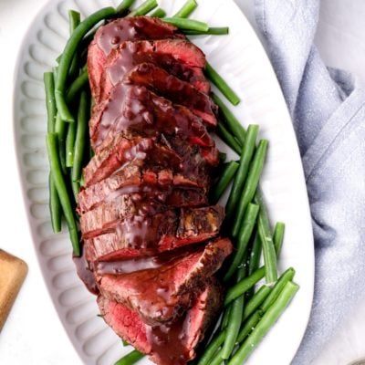 Platter of roast beef tenderloin with red wine sauce over green beans.