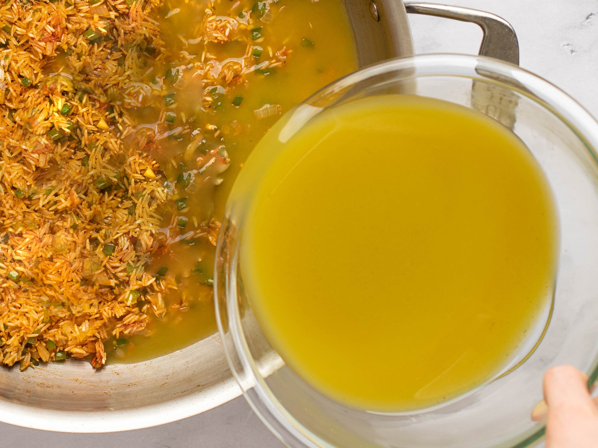 Chicken broth pouring into a pot of rice.