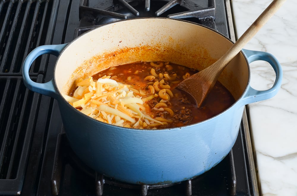 adding the cheese and evaporated milk to the chili mac