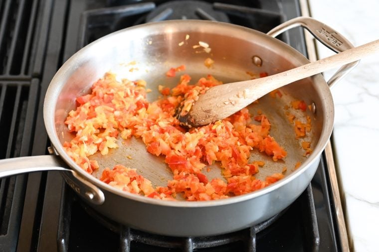 Wooden spoon stirring softened veggies in a skillet.