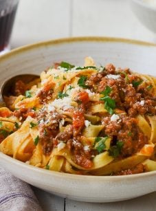Bolognese with pasta in bowl with glass of wine