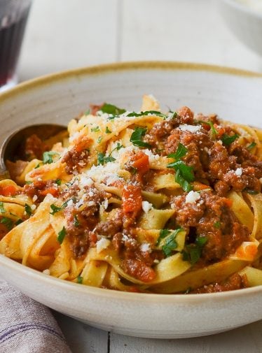 Bolognese with pasta in bowl with glass of wine