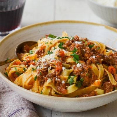 Bolognese with pasta in bowl with glass of wine