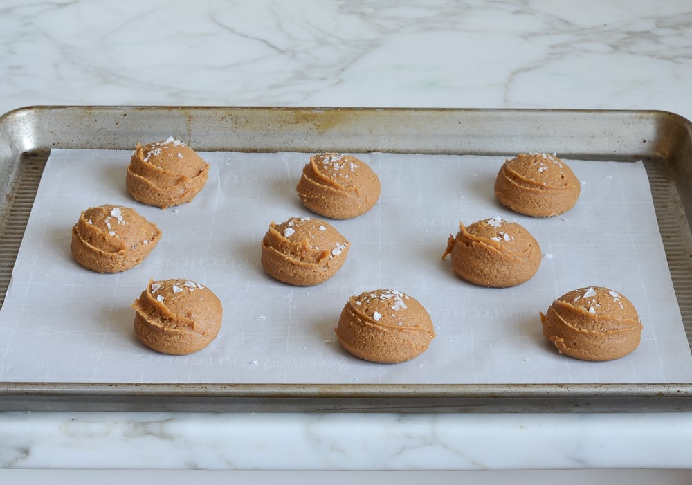 Scoops of flourless peanut butter cookie dough on a lined baking sheet.